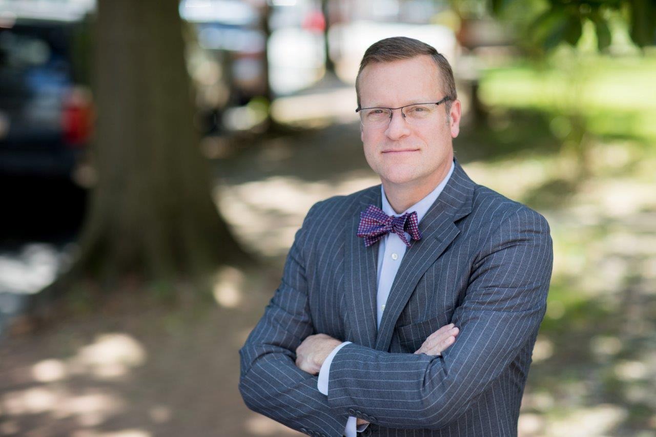 Attorney Tim Rayne posing in a suit and bow tie outdoors.